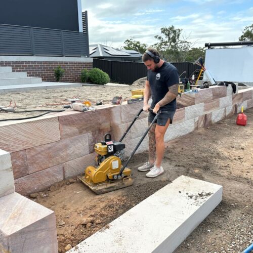 sydney landscaper compacting soil near sandstone retaining wall